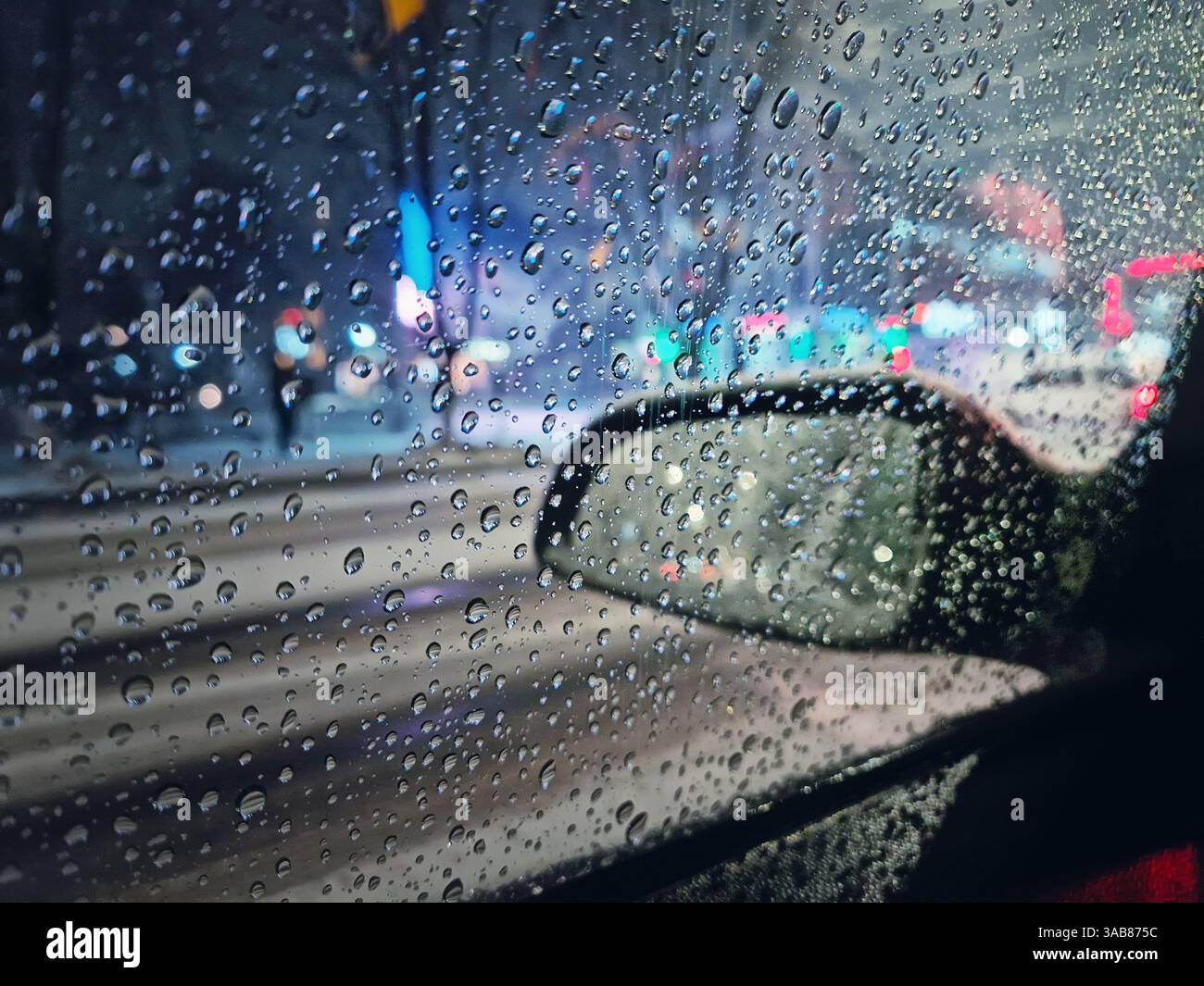 Neve fusa e nevischio cadono sul finestrino dell'auto con vista sullo specchietto laterale. Scena urbana notturna d'inverno - Immagine stock catturata con smartphone
