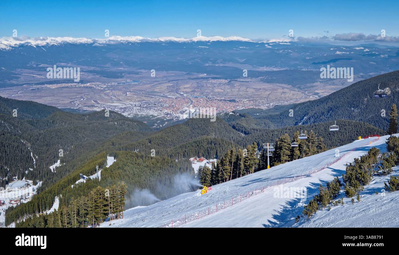 Località sciistica di Bansko sui monti Pirin con seggiovie che si spostano sopra le piste innevate e una vista panoramica sulle colline fino al centro storico - Immagine stock catturata con smartphone