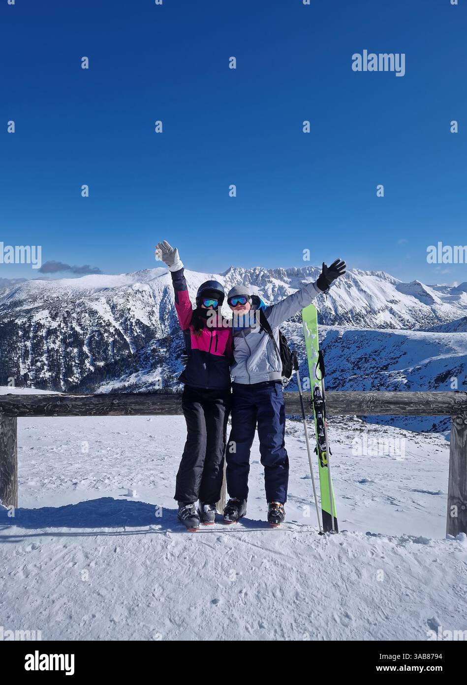 Coppia felice in piedi sulla cima innevata della montagna con le braccia sollevate che si pongono come un'ondata di macchina fotografica. Gli sciatori uomini e donne praticano sport invernali insieme havi - Immagine stock catturata con smartphone