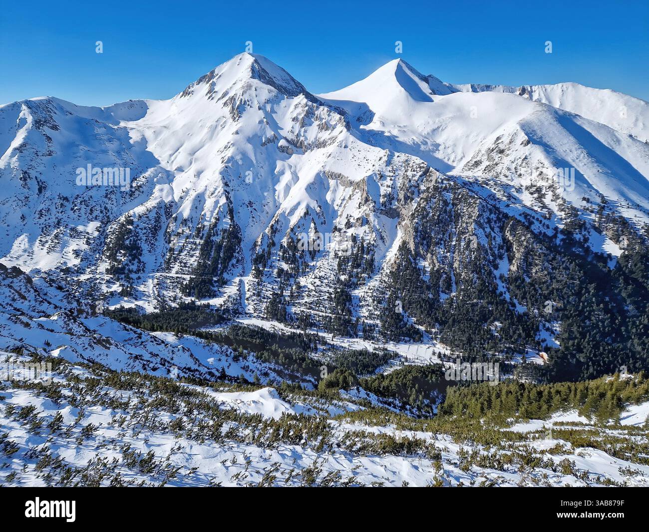 Vista aerea sopra il crinale dei Pirin con cime rocciose ricoperte di neve. Vista invernale della stazione sciistica di Bansko in Bulgaria - Immagine stock catturata con smartphone