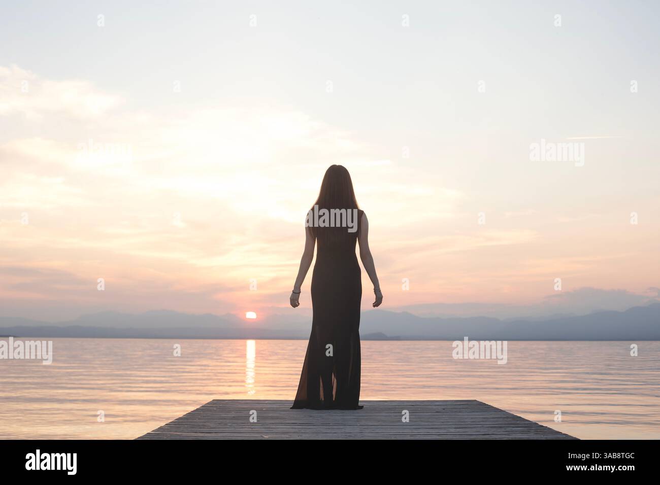 donna in nero contempla il mare al tramonto dal molo Foto Stock