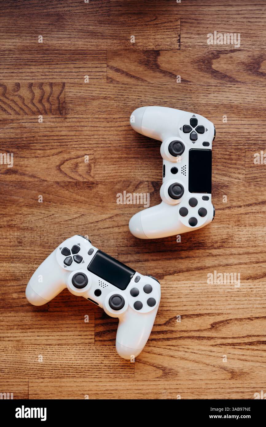 Due controller di gioco bianchi si trovano su una superficie in legno, evidenziando un design elegante e una tecnologia moderna, perfetti per esperienze di gioco interattive e. Foto Stock