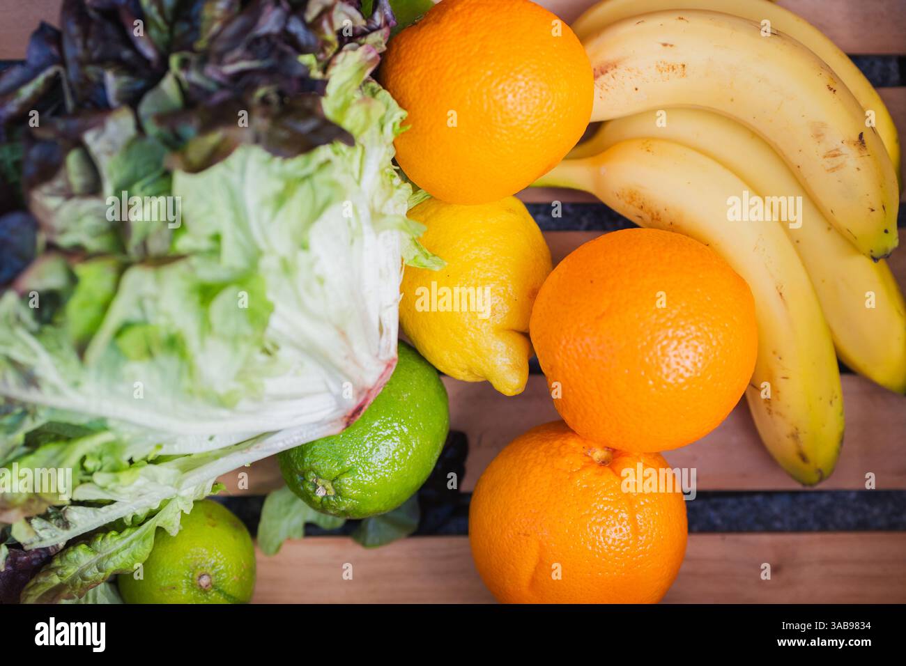 Una vivace esposizione di frutta e verdura, tra cui lattuga, arance, banane, limes, e limoni, disposti su un tavolo di legno. Perfetto per una sana ea Foto Stock