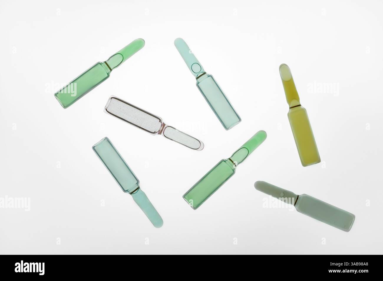 Una collezione di fiale di vetro verdi e gialle sparse su una superficie bianca. Queste fiale mediche contengono varie soluzioni liquide e sono utilizzate in hea Foto Stock