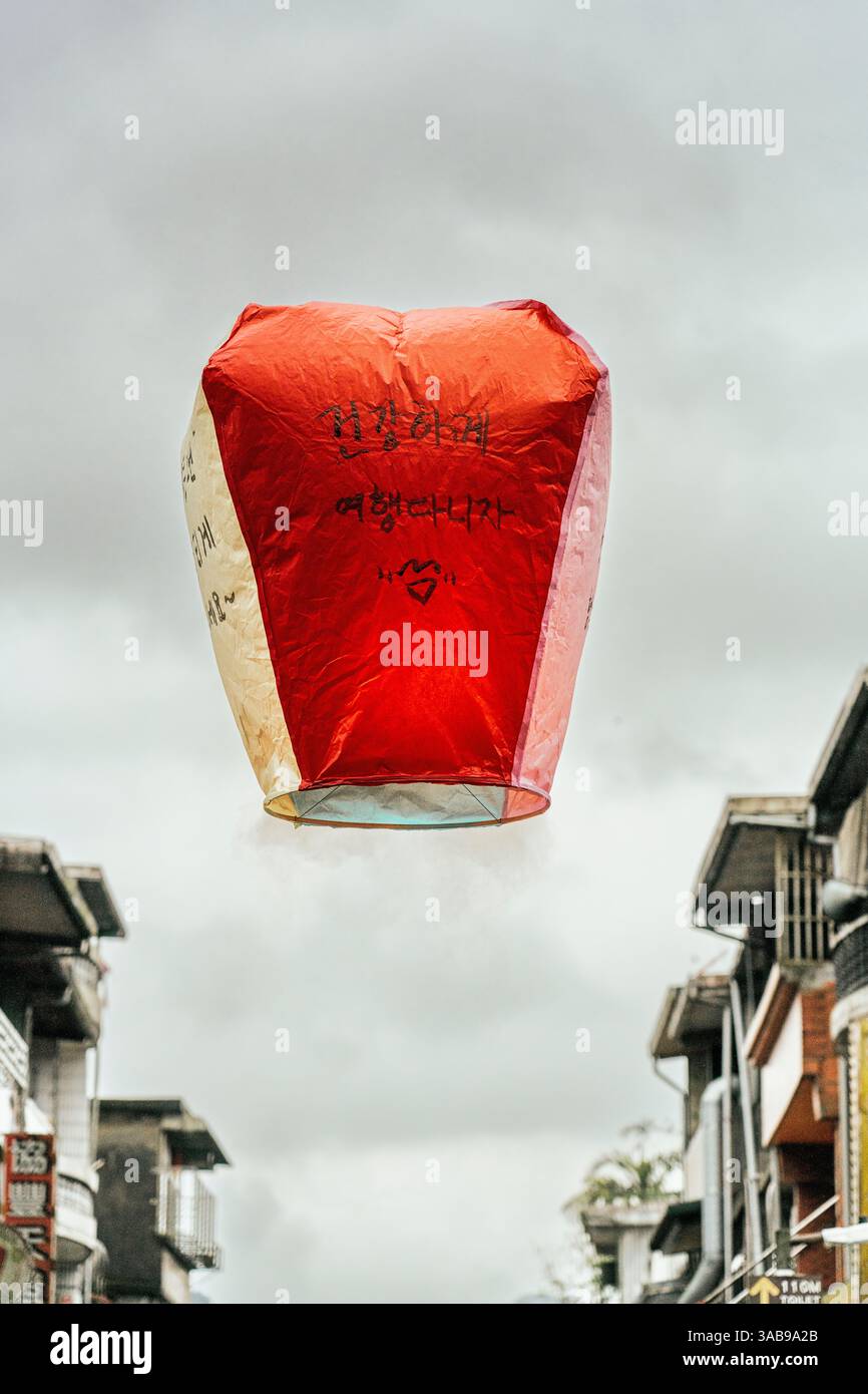 Una lanterna di carta cinese rossa sale contro un cielo nuvoloso, adornata con frasi scritte a mano in inchiostro nero. A Taiwan, questa lanterna tradizionale Foto Stock