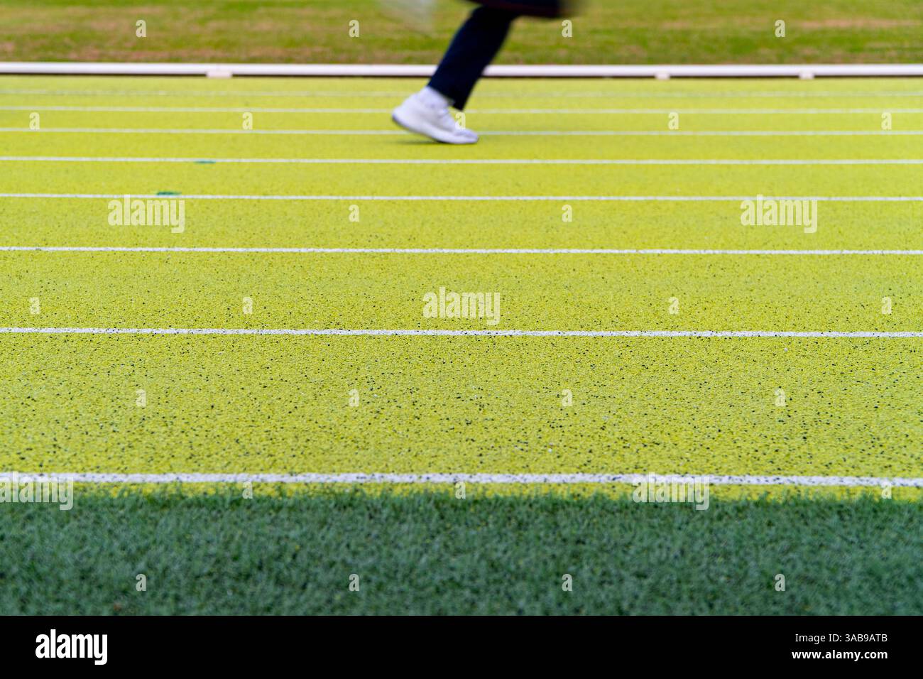 Vista corta e irriconoscibile di un atleta che corre su una vivace pista da running verde in uno stadio di atletica all'aperto. L'attenzione è rivolta alle scarpe atletiche Foto Stock