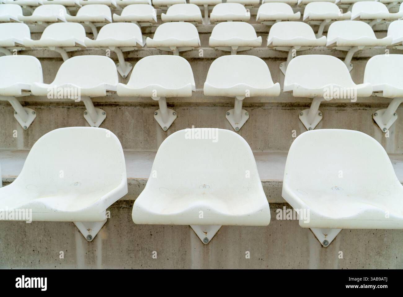 Una sezione di sedili bianchi vuoti e intemprati disposti in fila in uno stadio di atletica all'aperto, che sottolinea la quiete e la quiete di un'attività fuori stagione o no Foto Stock