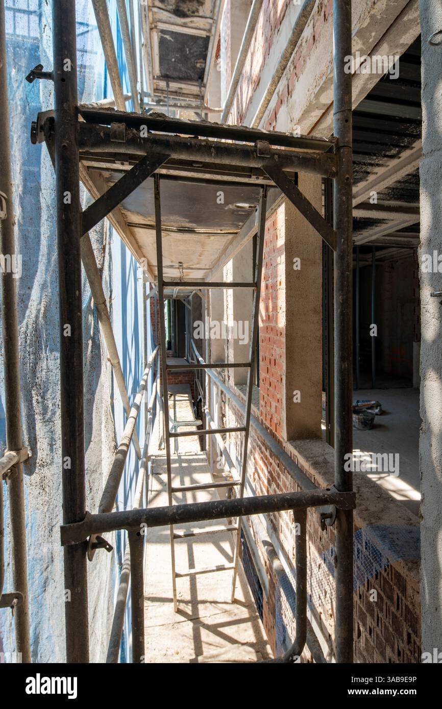 Ponteggi illuminati dal sole delimitano la stretta passerella di un cantiere, fiancheggiata da pareti in mattoni a vista. Il framework indica lo sviluppo di edifici in corso Foto Stock