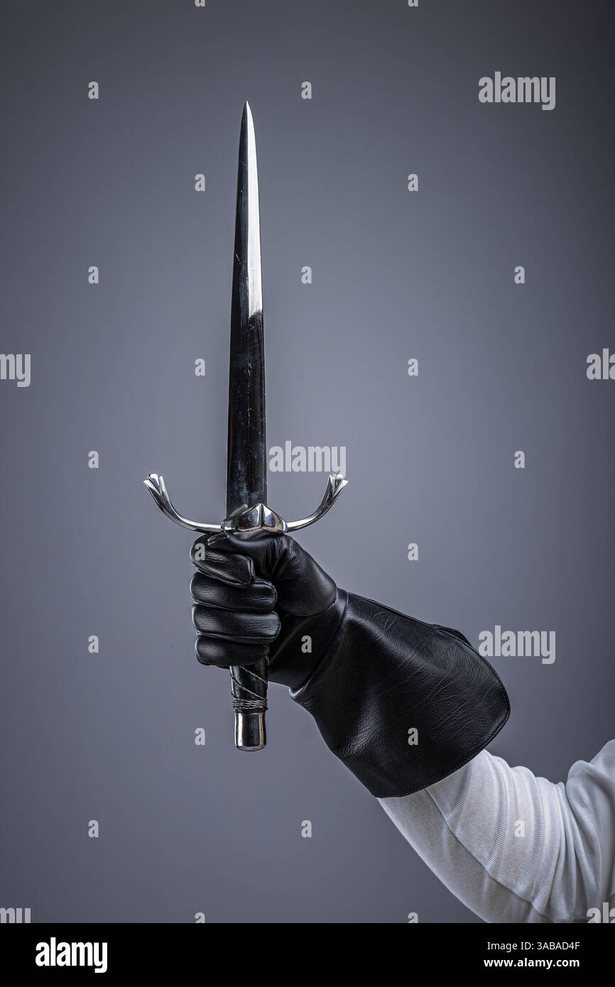 Guanto per impugnare Sharp Medieval Dagger. Primo piano di una mano in un guanto di pelle che afferra una lama appuntita. Foto Stock