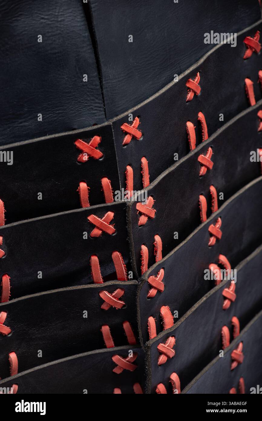 Primo piano della allacciatura Armor in pelle nera e rossa. Vista dettagliata dell'intricata allacciatura rossa che collega le piastre in pelle nera del cuirass medievale. Foto Stock