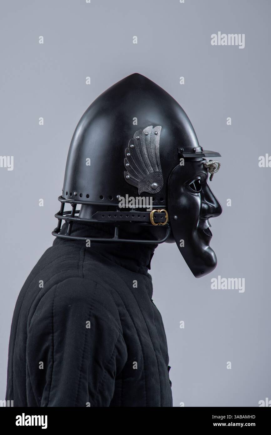 Elmetto in acciaio nero con maschera facciale. Protezione per la testa grottesca medievale con ali decorative. Foto Stock