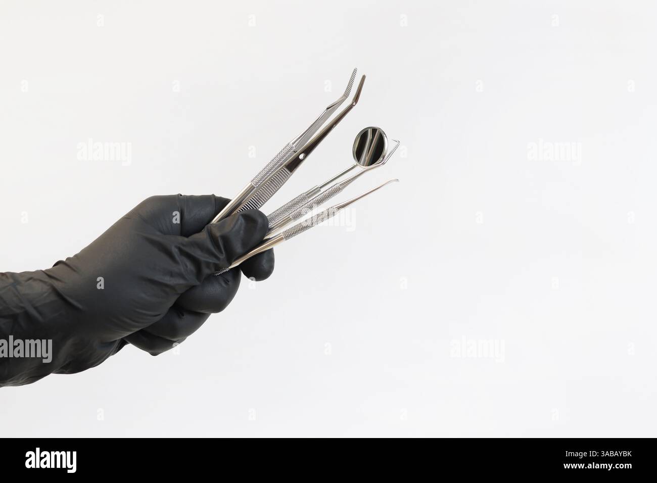 Strumento dentale nelle mani di un dentista, primo piano. Specchio dentale, pinzette e ganci utilizzati nel trattamento di varie malattie dei denti e GU Foto Stock