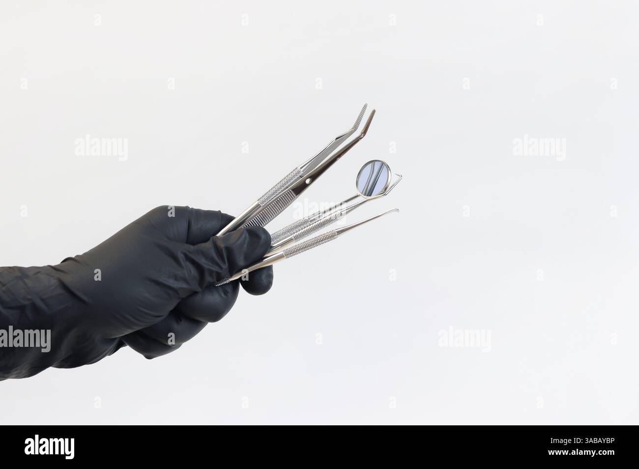 Strumento dentale nelle mani di un dentista, primo piano. Specchio dentale, pinzette e ganci utilizzati nel trattamento di varie malattie dei denti e GU Foto Stock