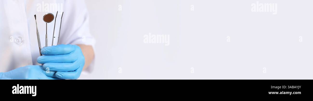 Strumento dentale nelle mani di un dentista, primo piano. Specchio dentale, pinzette e ganci utilizzati nel trattamento di varie malattie dei denti e GU Foto Stock