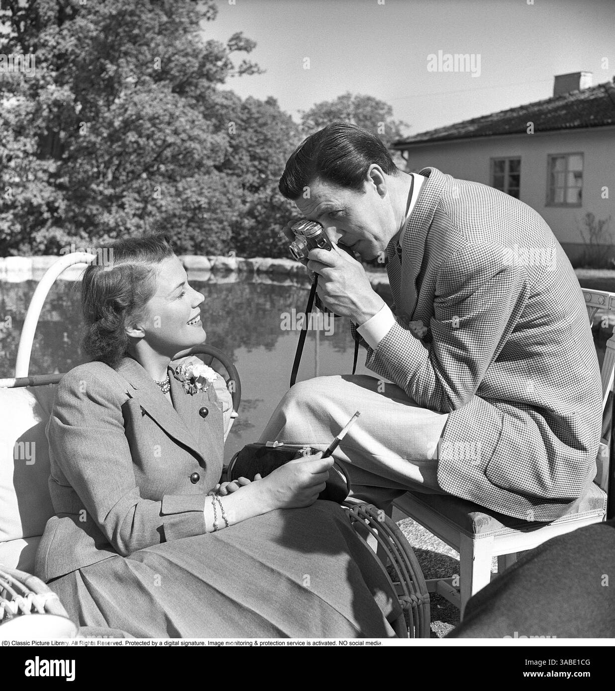 In posa per una foto 1955. L'attrice Sickan Carlsson (1915-2011) posa per Karl-Arne Holmsten (1911-1995) che sta scattando una sua fotografia con una macchina fotografica analogica. È vestita con una tuta formale, tenendo in mano un portasigarette e una piccola borsetta. Svahn Foto Stock In posa per una foto 1955. L'attrice Sickan Carlsson (1915-2011) posa per Karl-Arne Holmsten (1911-1995) che sta scattando una sua fotografia con una macchina fotografica analogica. È vestita con una tuta formale, tenendo in mano un portasigarette e una piccola borsetta. Svahn Foto Stock
