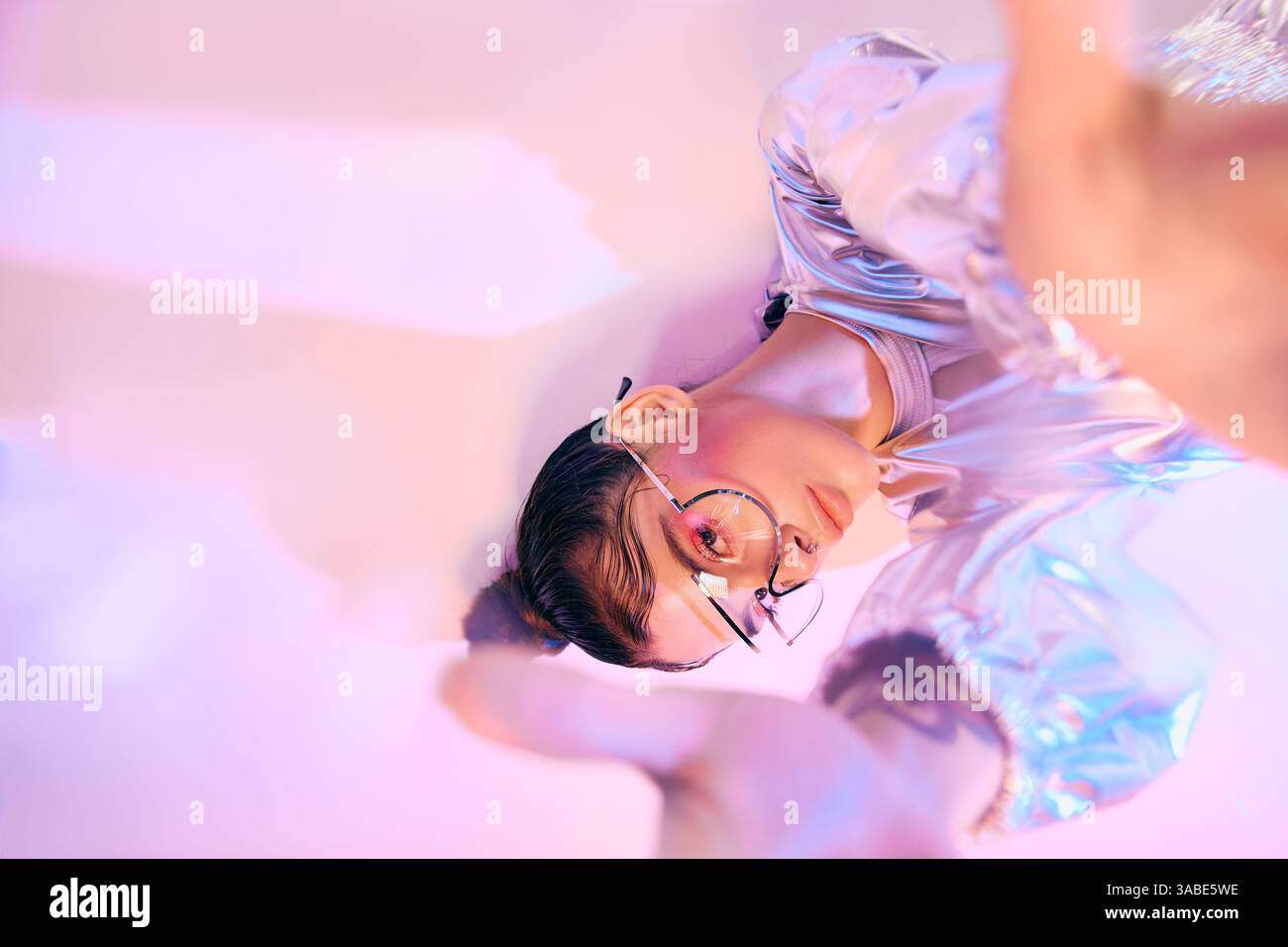 La donna elegante sfoggia il suo abbigliamento futuristico che mescola colori olografici sotto un'illuminazione soffusa Foto Stock