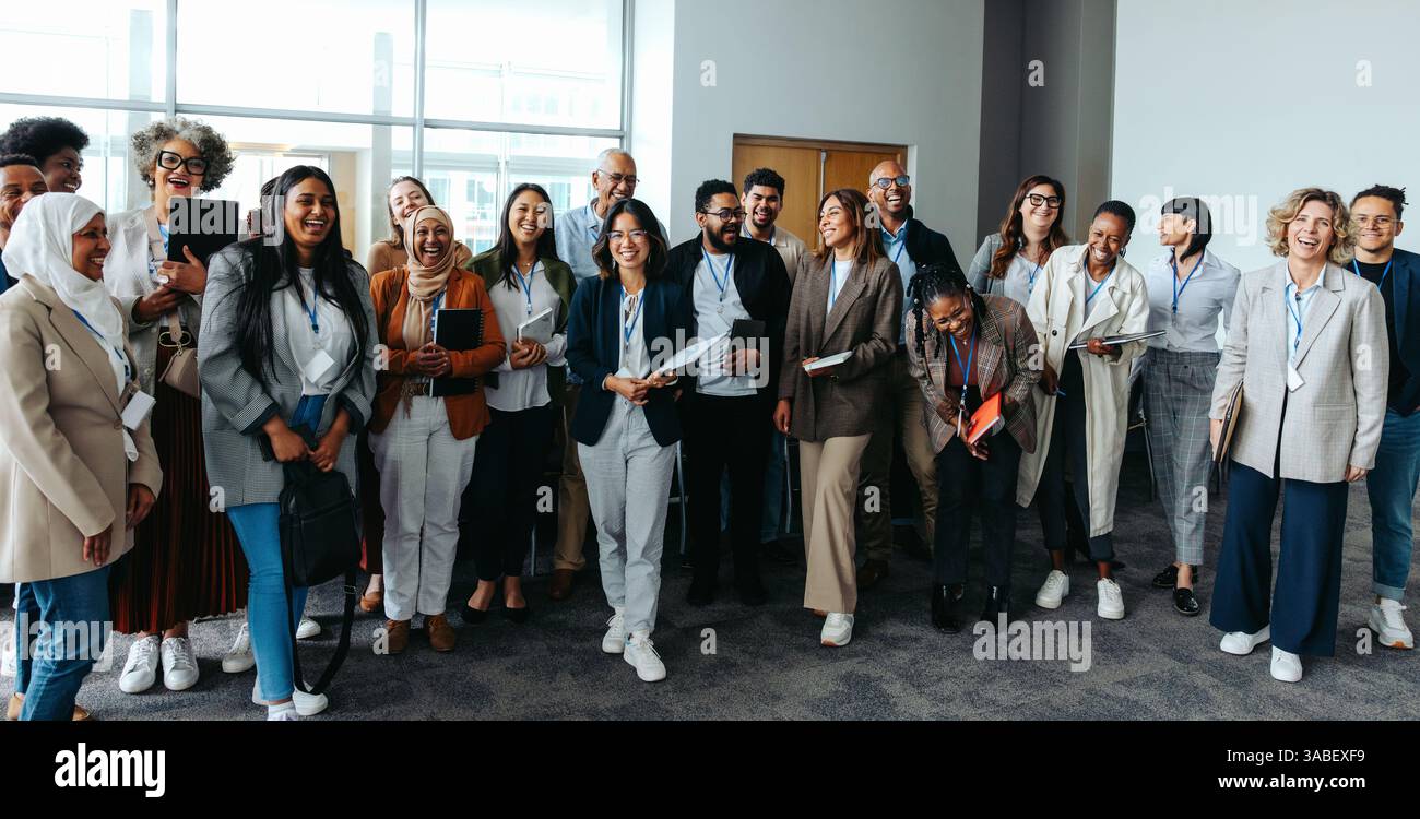 Gruppo di professionisti che sorridono e ridono durante una riunione d'affari. L'ambientazione è informale e rappresenta la collaborazione, la diversità e il lavoro di squadra. Foto Stock