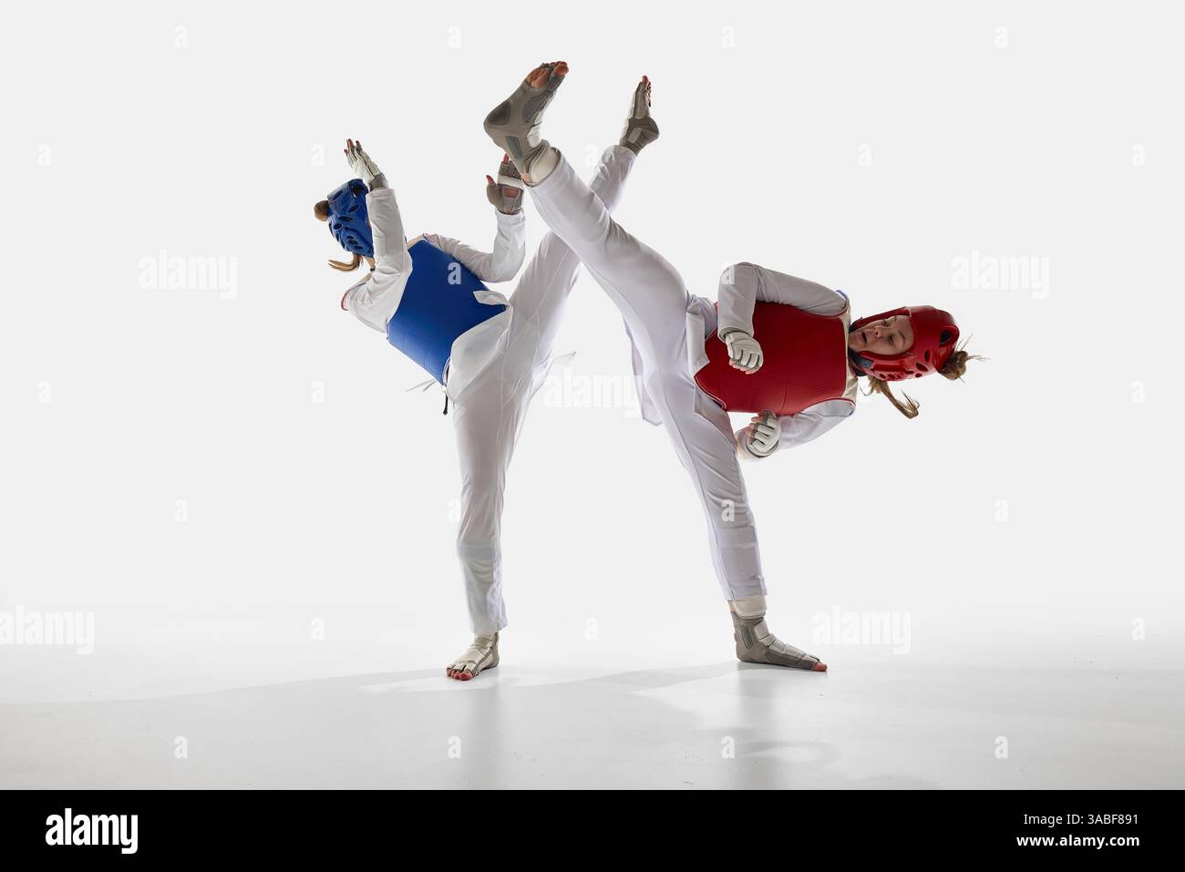 Due atlete di taekwondo in movimento, che combattono con calci sincronizzati sullo sfondo bianco dello studio. Foto Stock