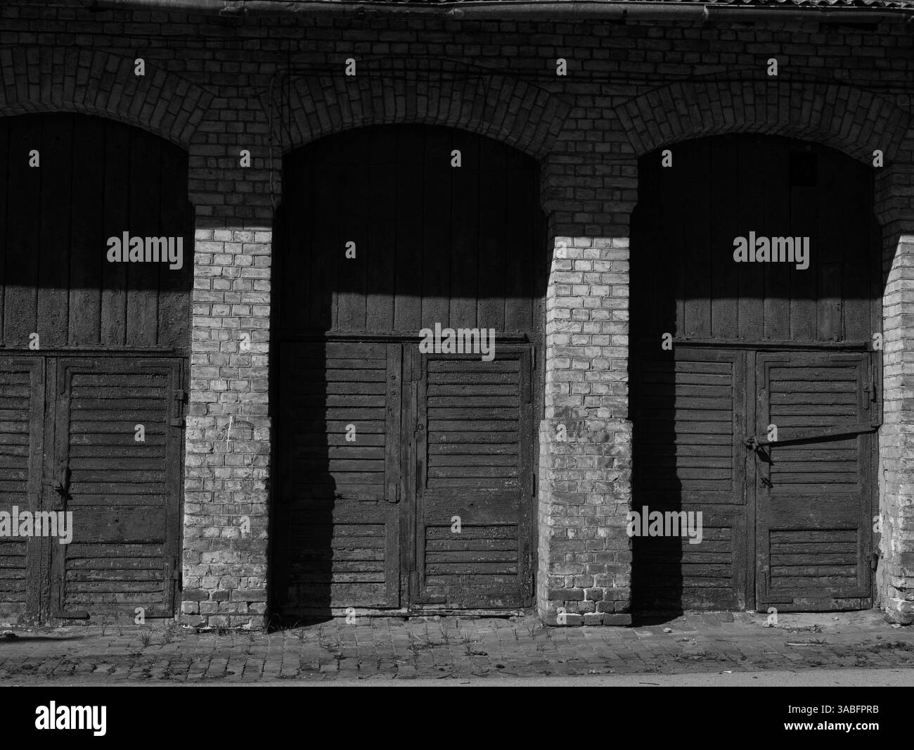 Vecchio edificio in mattoni con porte in legno intemperie alla luce calda del sole. Foto Stock