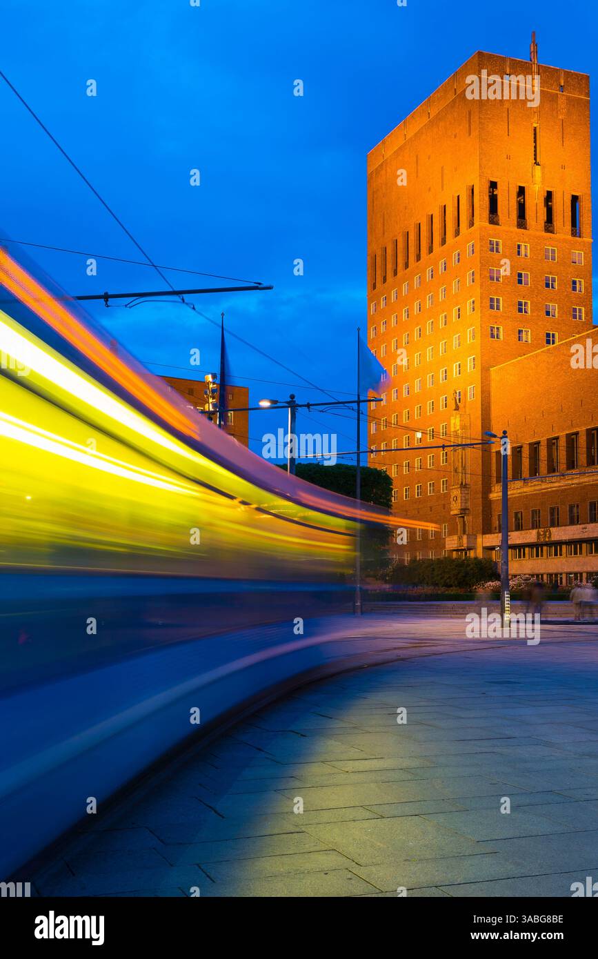 Oslo, Norvegia notturna, vista notturna di un tram cittadino che accelera verso l'edificio del Municipio (Radhus) nel quartiere portuale centrale di Oslo, Norvegia. Foto Stock