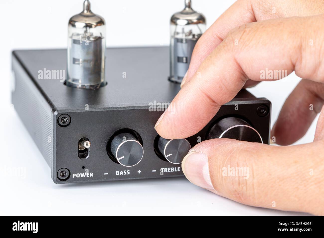 Messa a punto di un amplificatore con tubo a vuoto: Immagine mirata di una persona che regola la manopola degli alti su un amplificatore nero, sottolineando precisione e controllo. Foto Stock
