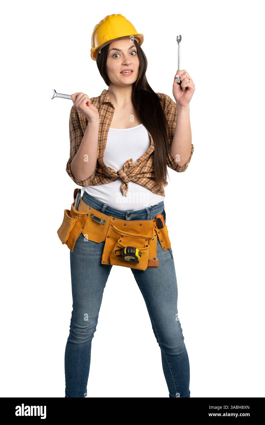 Una lavoratrice edile con un elmetto giallo e una camicia a quadri contiene due chiavi con un'espressione confusa, che simboleggiano l'indecisione o il problem-solv Foto Stock