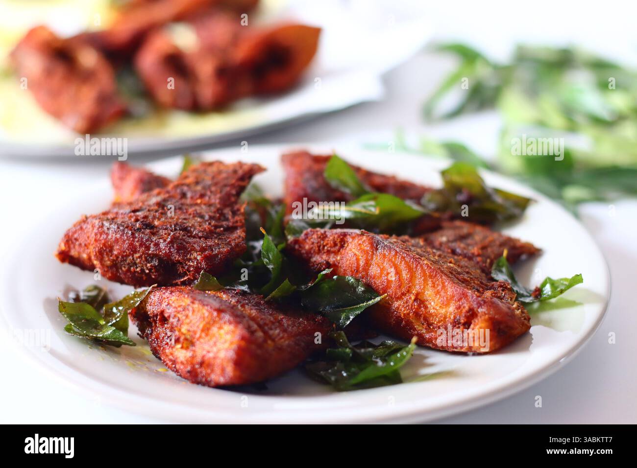 Pesce spot di perle del Vietnam marinato con spezie aromatiche e fritto alla perfezione dorata, guarnito con foglie di curry fresco. Acquisito da un'ang superiore Foto Stock