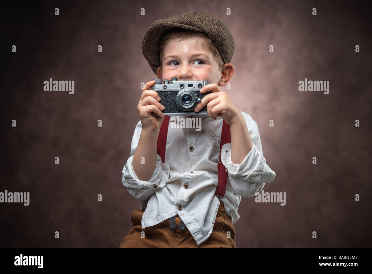 Fotografo ragazzo con fotocamera retrò che crea immagini su sfondo vintage Foto Stock