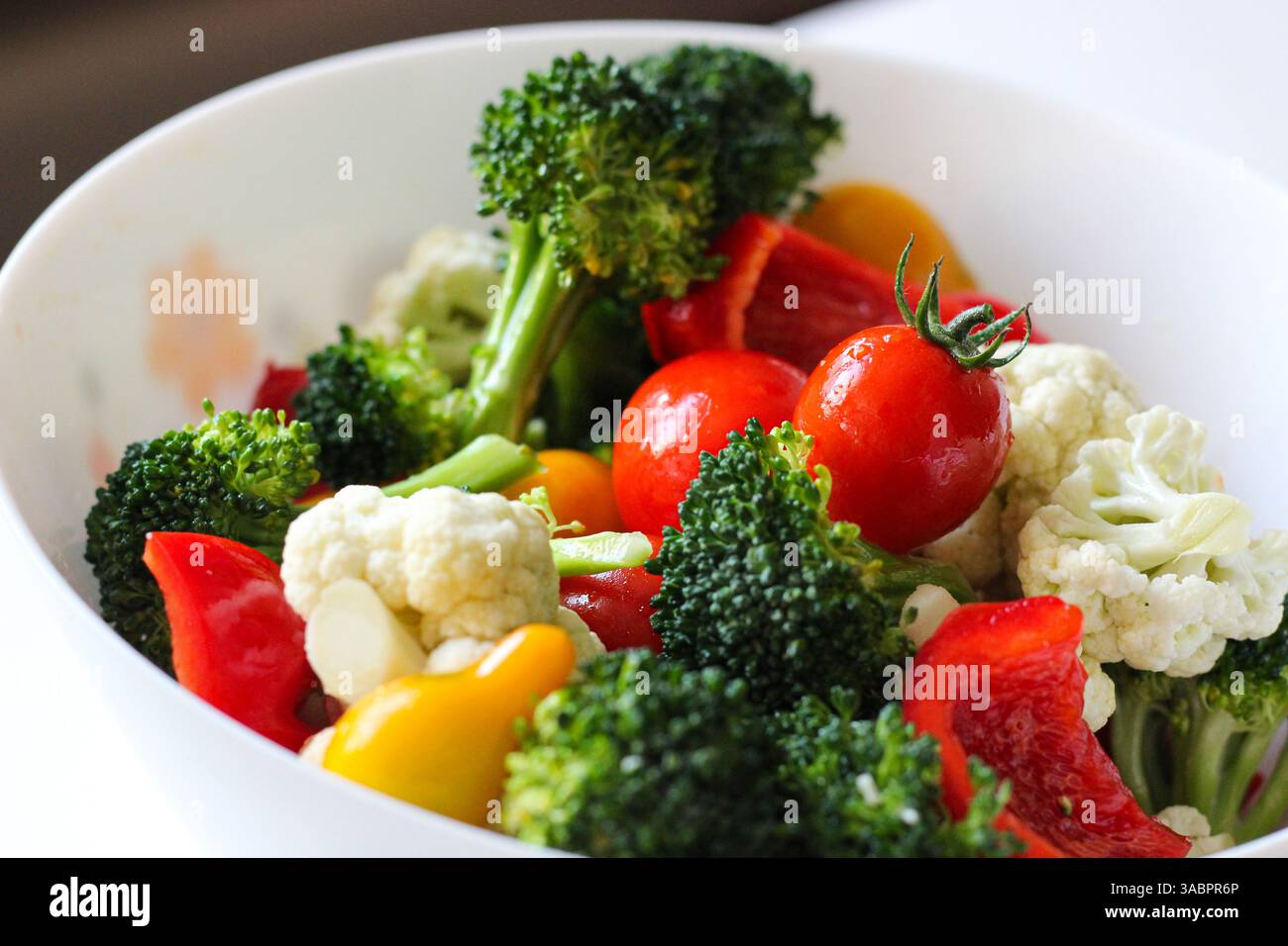 Vivace insalata di verdure fresche con broccoli, pomodori ciliegini, peperoni e cavolfiore in una ciotola bianca. Concetto di alimentazione sana Foto Stock