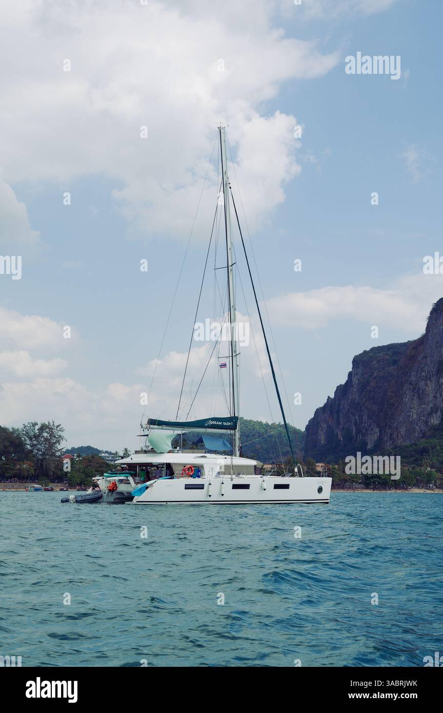Il catamarano di lusso galleggia vicino a una riva costeggiata da palme al largo di Krabi Foto Stock
