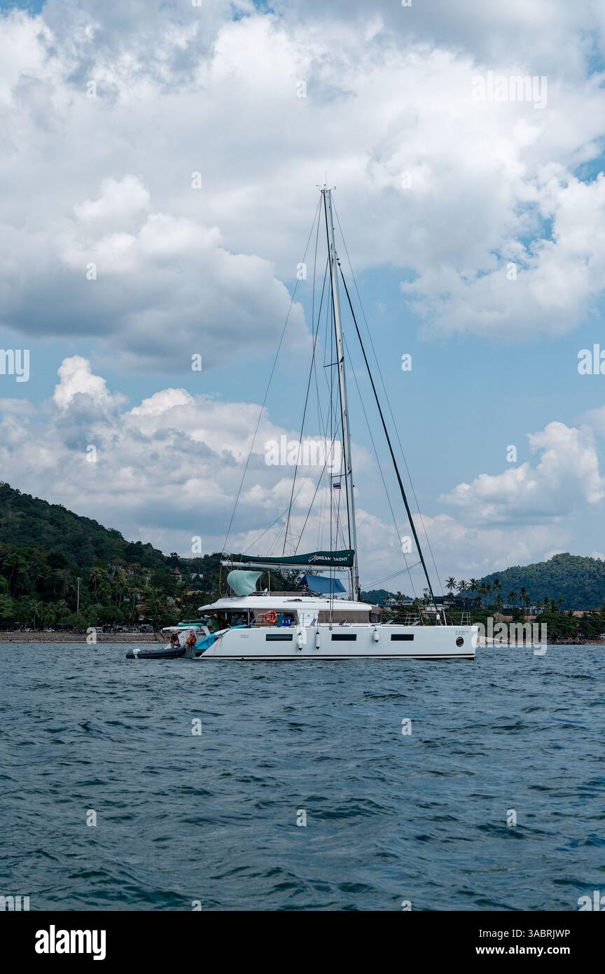 Il catamarano di lusso galleggia vicino a una riva fiancheggiata da palme a Krabi, sotto morbide nuvole Foto Stock