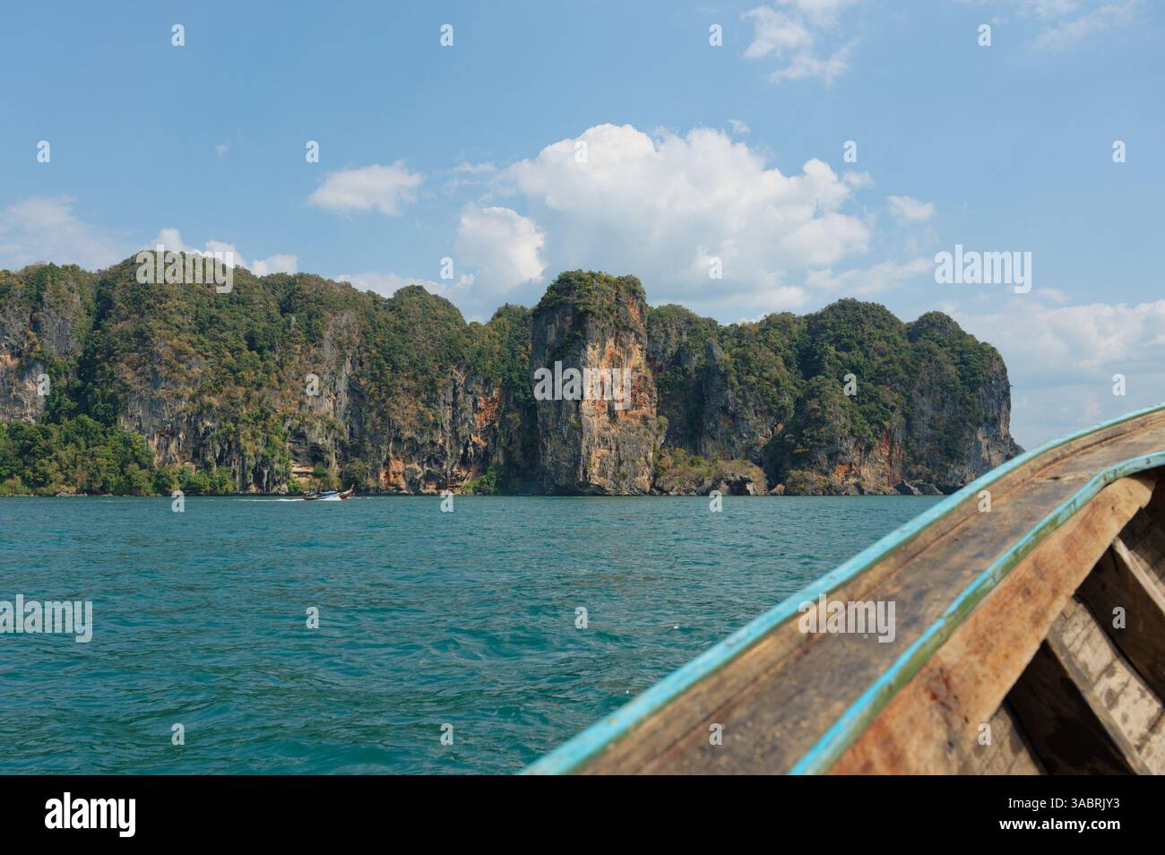 La barca a coda lunga in legno si avvicina alle imponenti scogliere calcaree di Krabi sotto un luminoso cielo tropicale Foto Stock