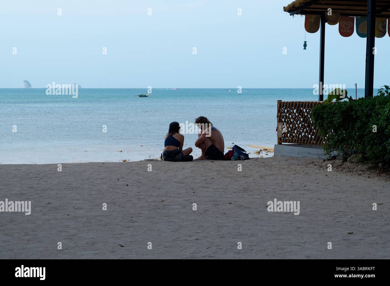 Due viaggiatori si siedono sul mare sulla spiaggia di Tonsai, condividendo un momento tranquillo Foto Stock