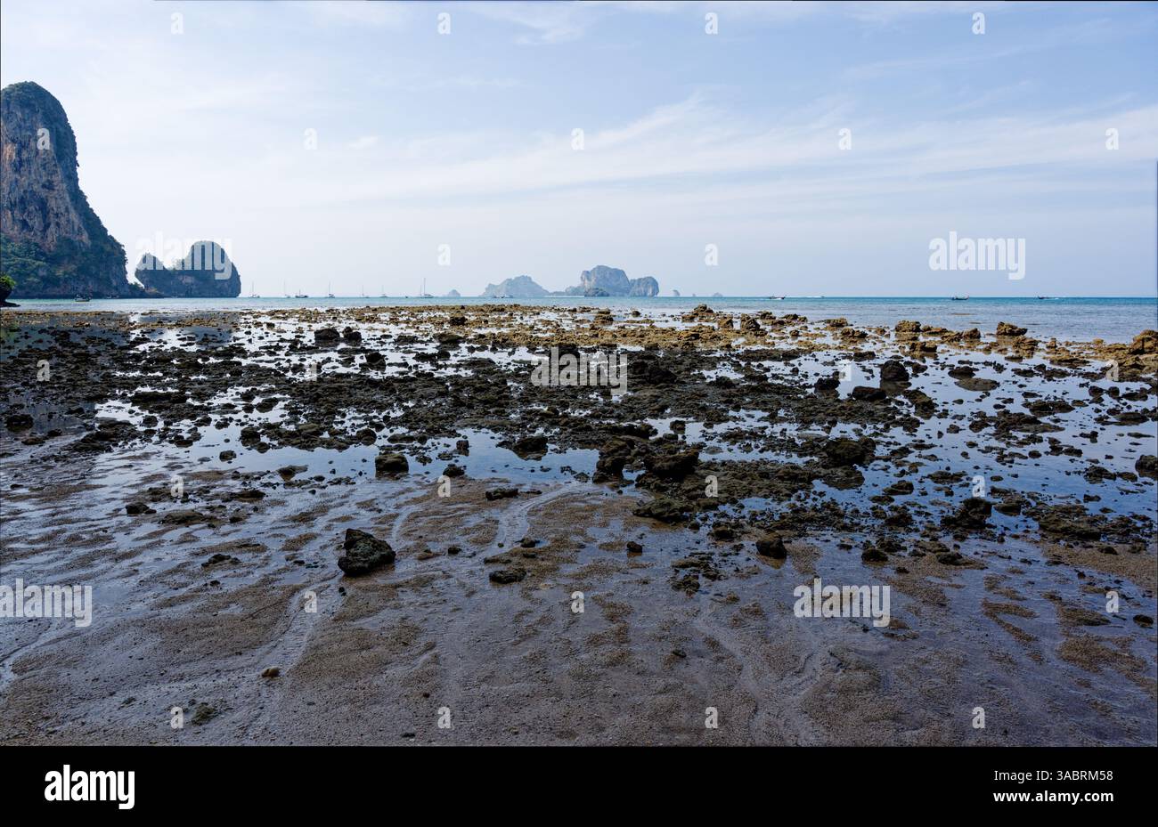 La bassa marea rivela una costa rocciosa sotto la luce del mattino, distanti scogliere calcaree che si innalzano dal Mare delle Andamane Foto Stock