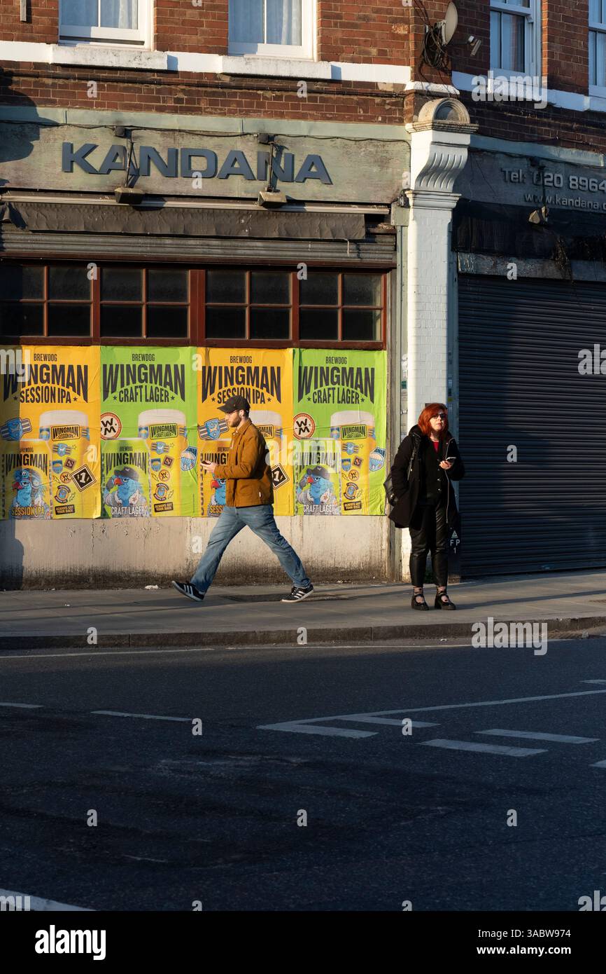 I pedoni passano davanti al pub Kandana, Londra, Regno Unito, con i poster della birra Wingman. Foto Stock