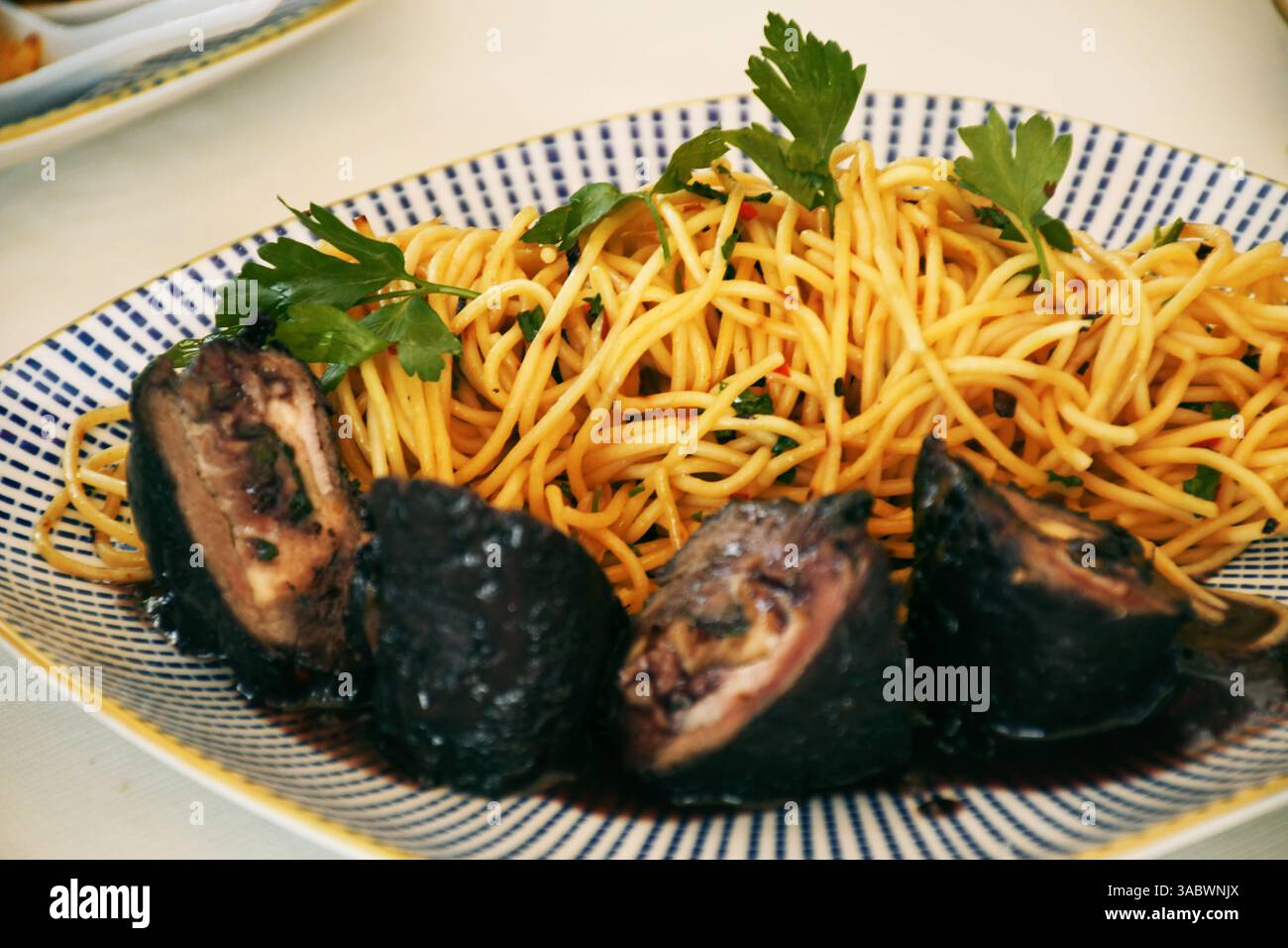 Piatto gourmet con spaghetti al dente, carne alla griglia e decorazioni in foglie verdi, condito con una salsa cremosa e brillante e uno sfondo blu, per creare Foto Stock