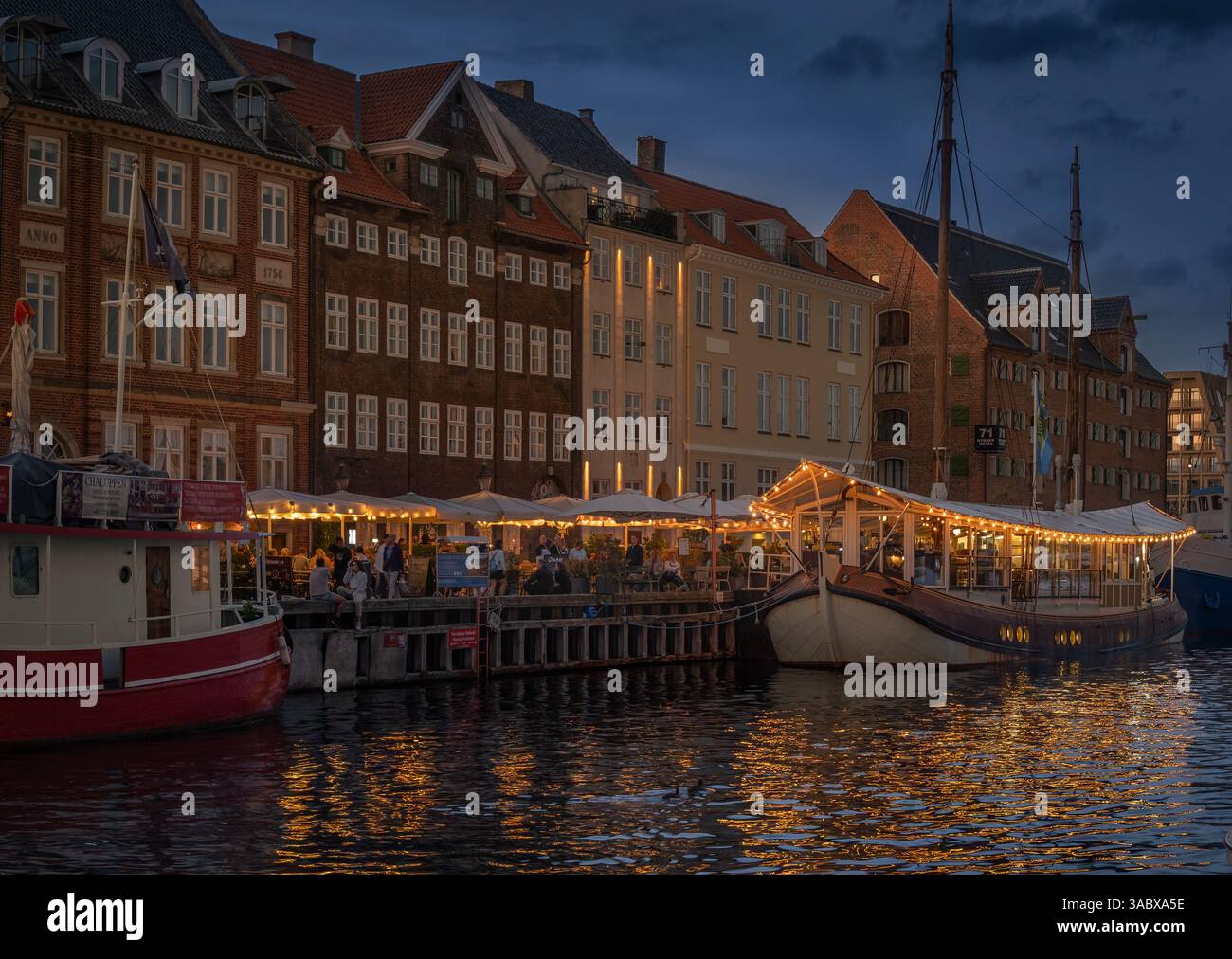 Splendida vista dei ristoranti galleggianti illuminati sul canale Nyhavn a Copenaghen, Danimarca, al crepuscolo in estate; riflessi in primo piano Foto Stock