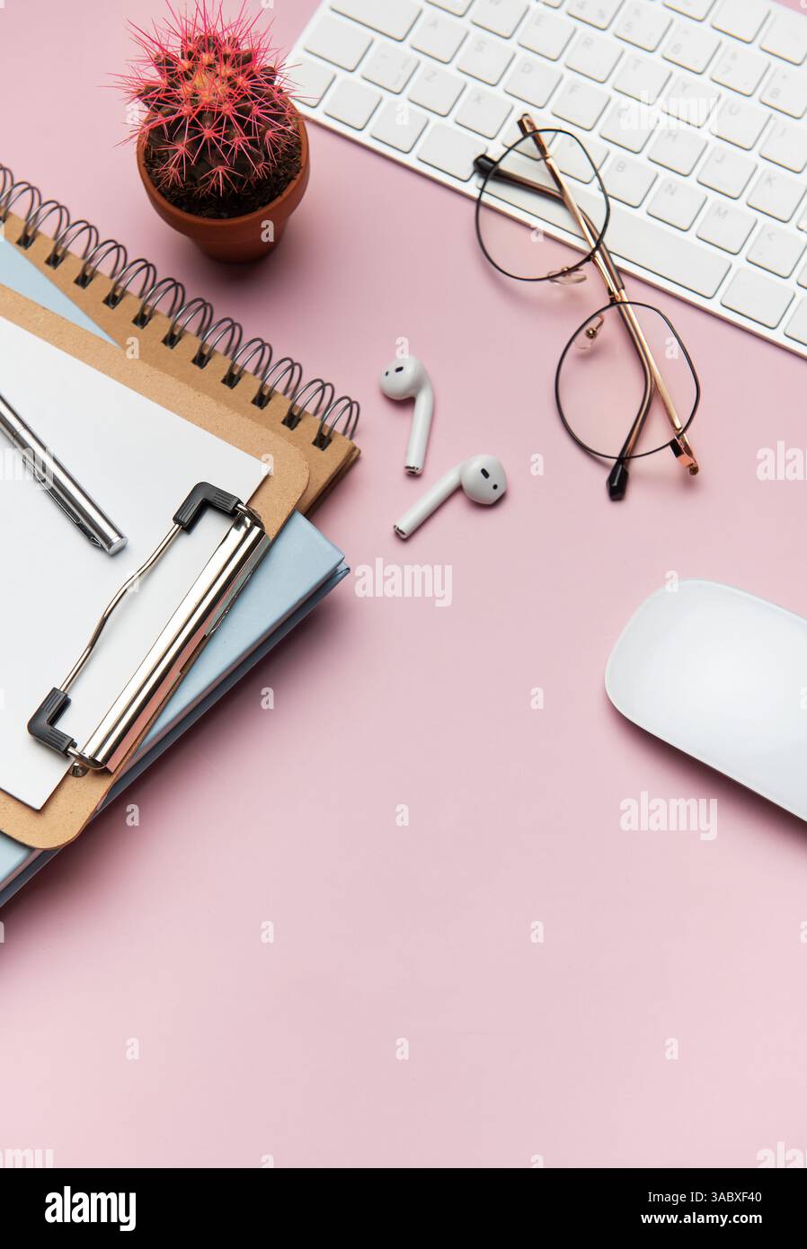 Forniture per ufficio e dispositivi tecnologici disposti in modo ordinato su un desktop rosa, creando uno spazio di lavoro ideale per la produttività e la concentrazione Foto Stock