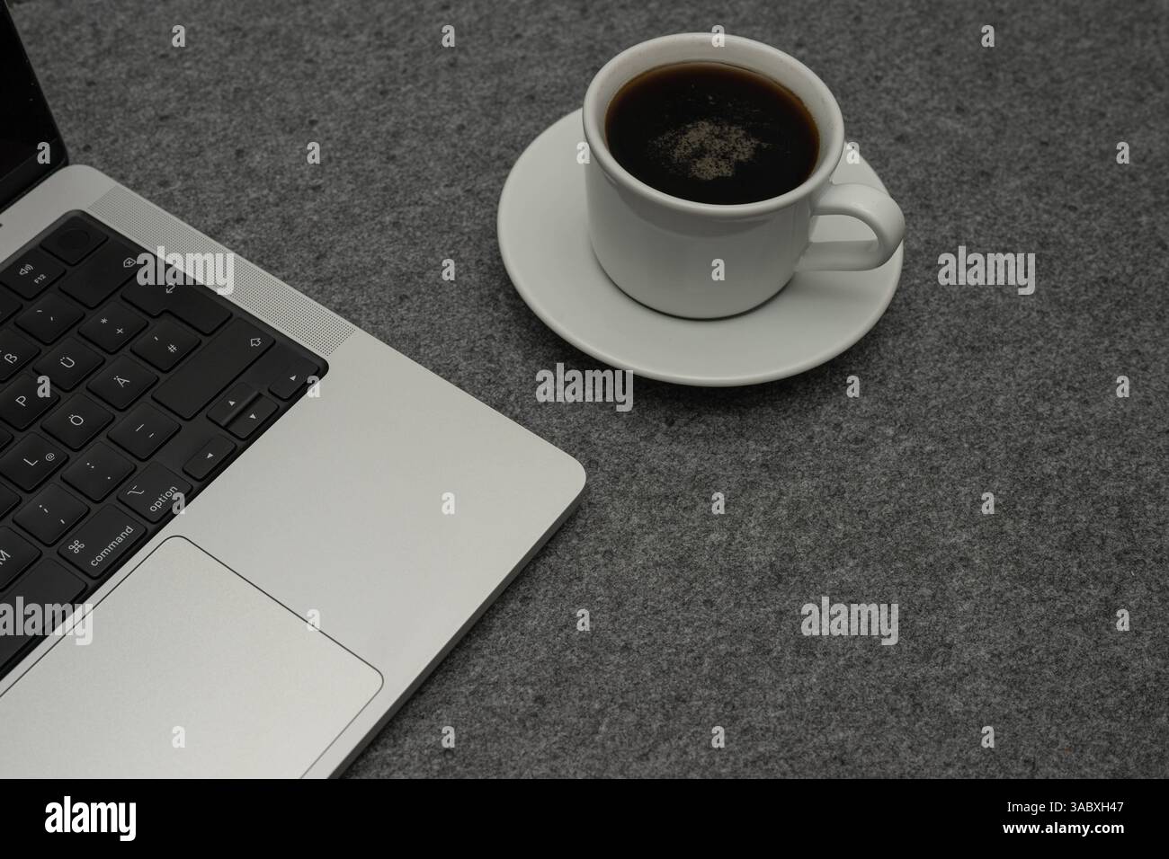 Laptop und Kaffeetasse auf grauem Filzhintergrund , Deutschland, 03.04.2025, Detailaufnahme eines modernen laptop neben einer Weißen Kaffeetasse mit schwarzem Kaffee auf einem grauen Filzuntergrund. Sistemazione DAS vermittelt eine ruhige Arbeitsatmosphäre im Homeoffice oder Büro. *** Laptop e tazza di caffè su sfondo grigio in feltro , Germania, 03 04 2025, primo piano di un computer portatile moderno accanto a una tazza di caffè bianco con caffè nero su sfondo grigio in feltro l'ambiente trasmette un'atmosfera di lavoro tranquilla in casa ufficio o ufficio Foto Stock