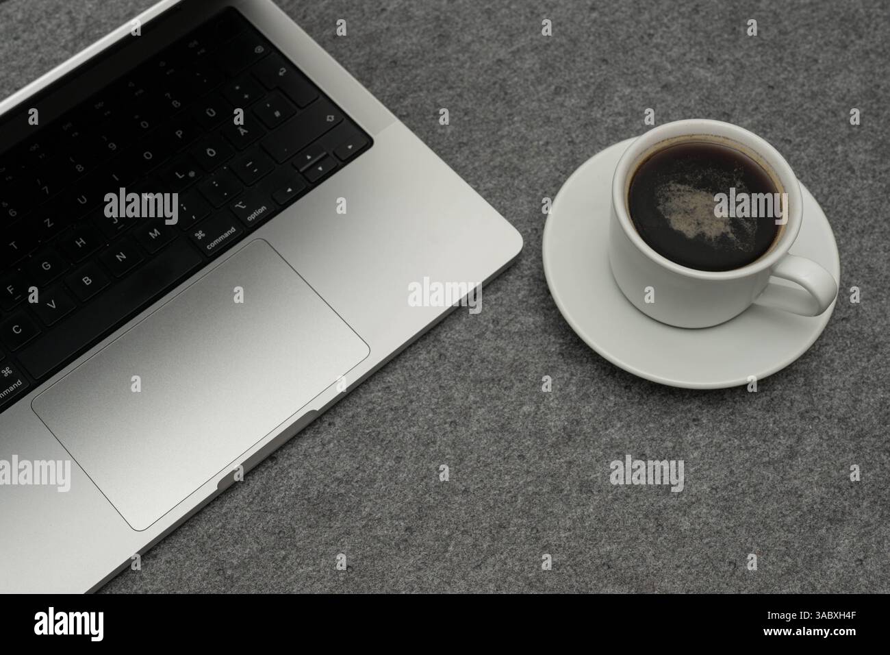 Laptop und Kaffeetasse auf grauem Filzhintergrund , Deutschland, 03.04.2025, Detailaufnahme eines modernen laptop neben einer Weißen Kaffeetasse mit schwarzem Kaffee auf einem grauen Filzuntergrund. Sistemazione DAS vermittelt eine ruhige Arbeitsatmosphäre im Homeoffice oder Büro. *** Laptop e tazza di caffè su sfondo grigio in feltro , Germania, 03 04 2025, primo piano di un computer portatile moderno accanto a una tazza di caffè bianco con caffè nero su sfondo grigio in feltro l'ambiente trasmette un'atmosfera di lavoro tranquilla in casa ufficio o ufficio Foto Stock