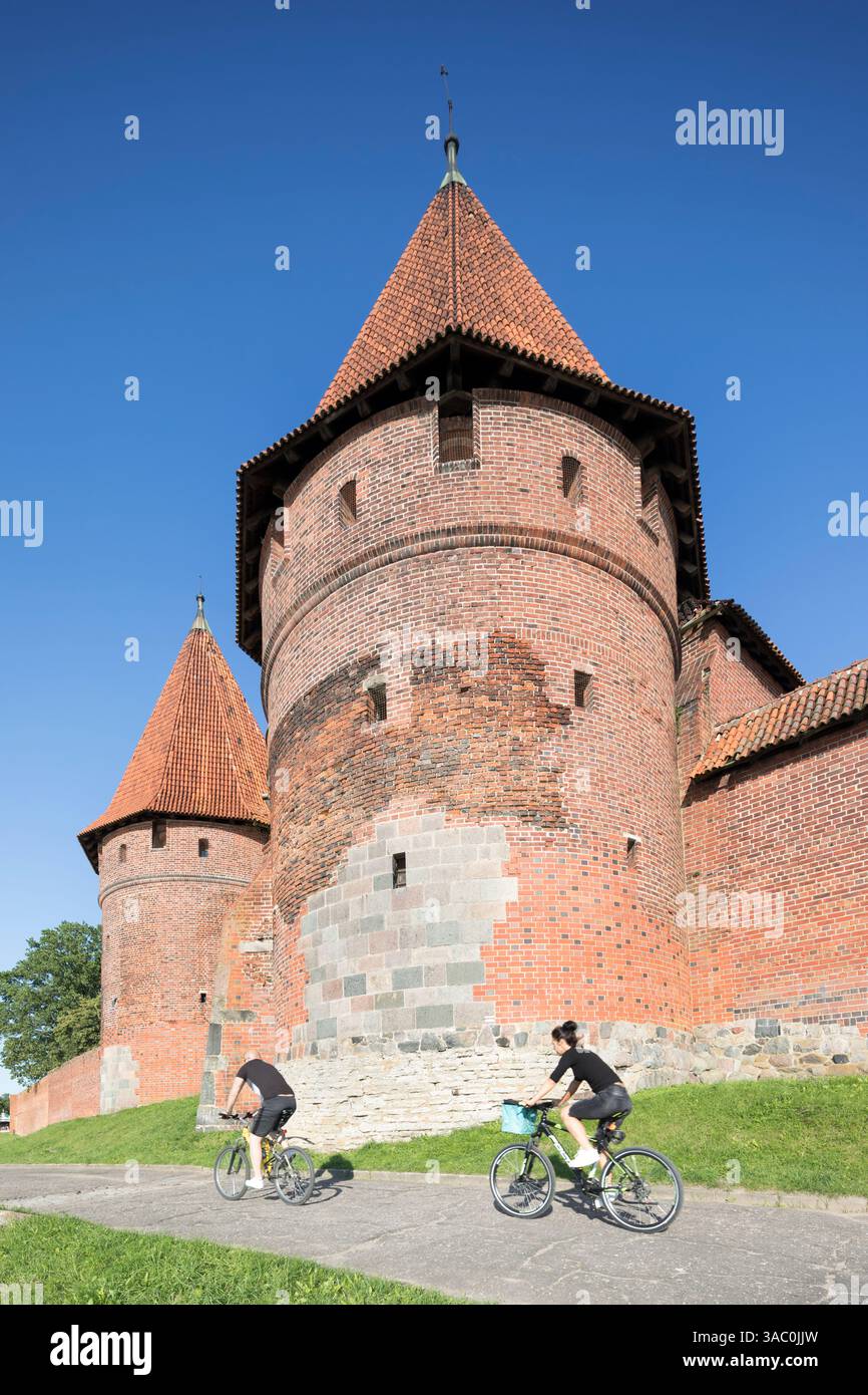 Polonia, Malbork, ciclisti che passano davanti alla torretta principale del castello di Malbork, uno dei più grandi castelli gotici d'Europa. Foto Stock