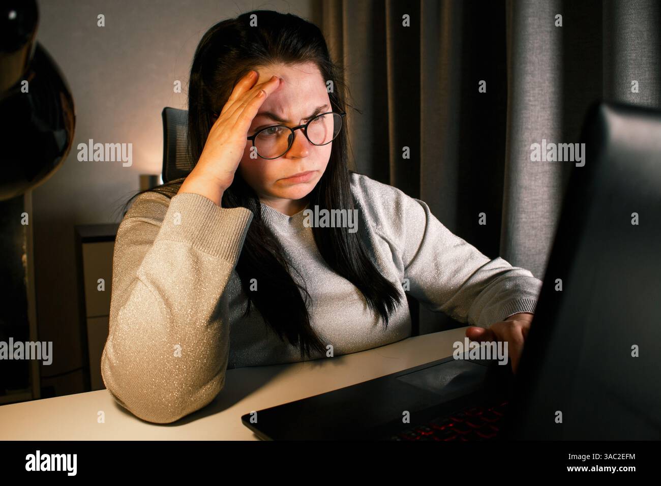 Una donna che lavora sodo lavora al computer nel suo ufficio domestico e cerca di risolvere i problemi di lavoro. Sentimento di disperazione e bruciati per problemi di lavoro Foto Stock