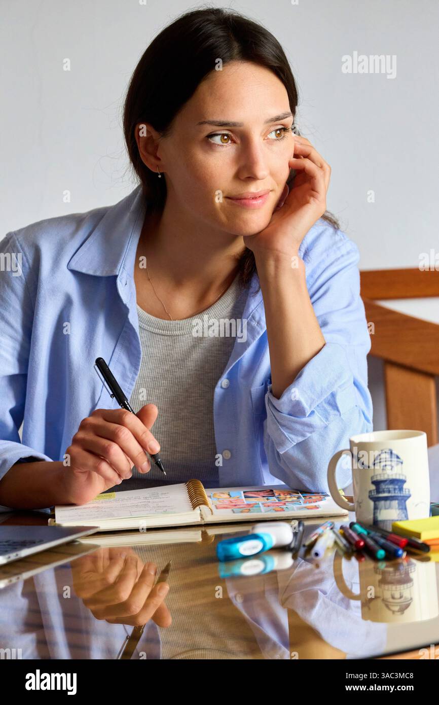 donna di 35 anni che studia a casa, guardando da un lato Foto Stock