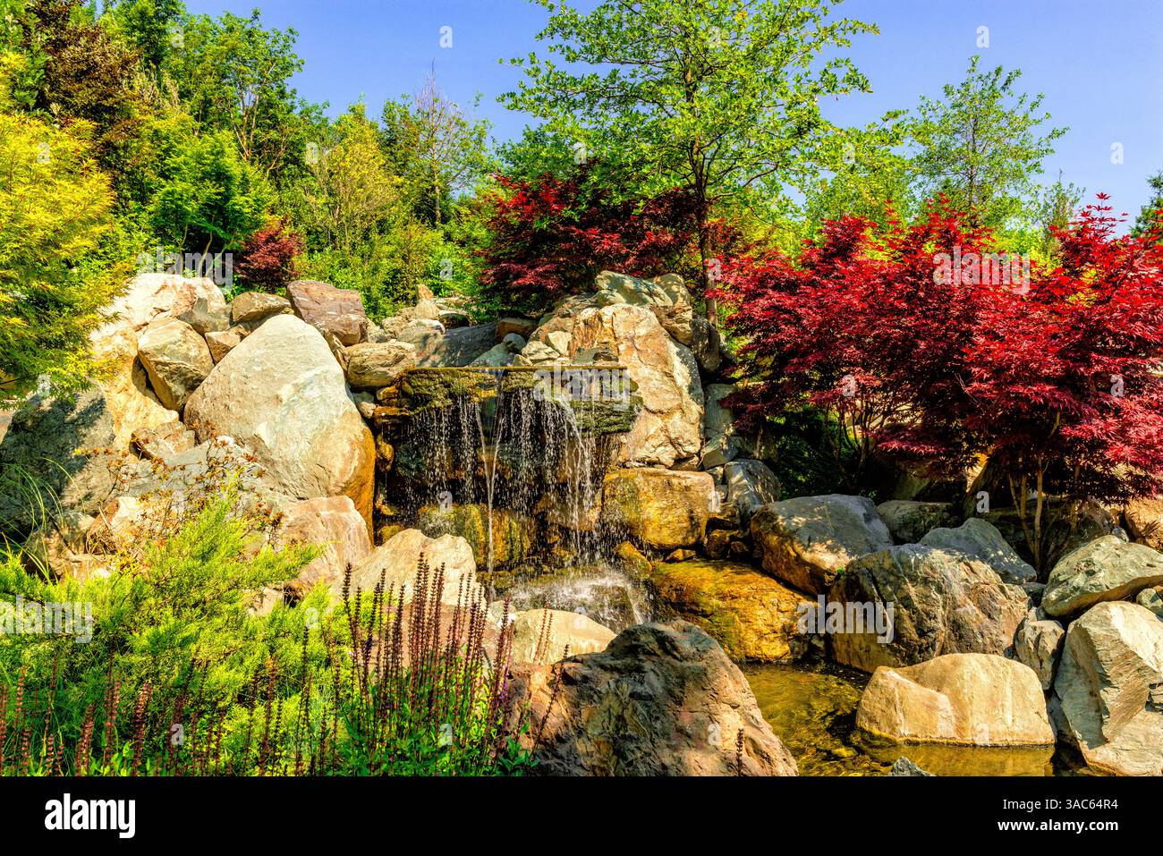 Splendido e luminoso paesaggio del parco pubblico gratuito della città con una cascata sul ruscello. Foto Stock