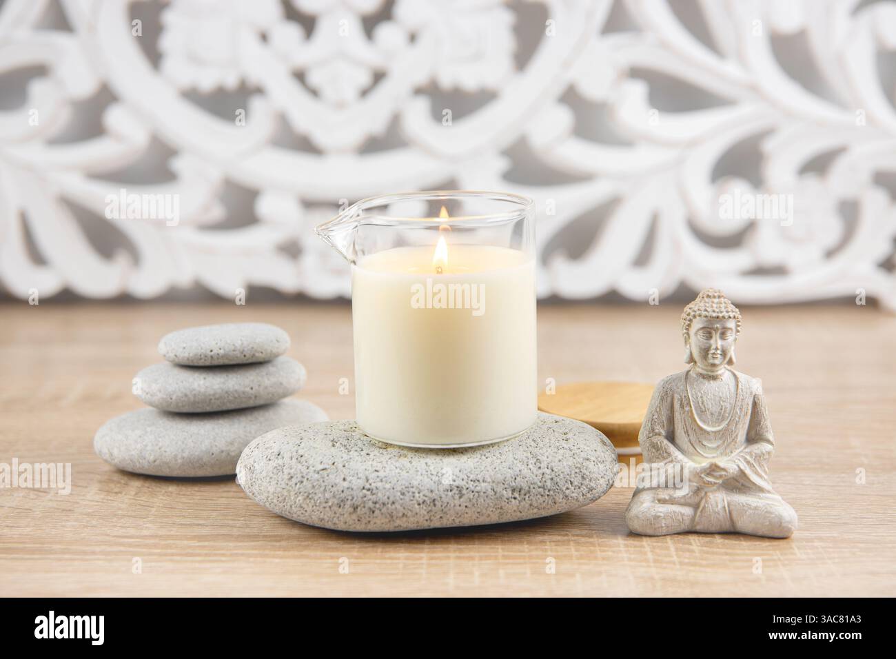 Candela profumata fatta in casa con olio per massaggi in tazza di vetro con beccuccio. Sfondo in stile boemo, statuetta di Buddha seduta, pietre zen impilate per rilassarsi. Foto Stock