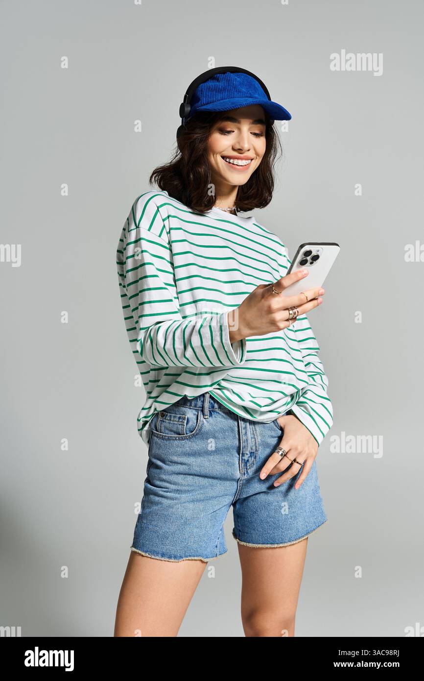 Una giovane donna con top a righe e pantaloncini in denim sorride al telefono, godendosi il sole estivo. Foto Stock