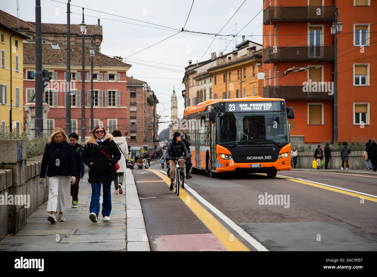 Strada trafficata della città con gente, moderno autobus arancione e architettura storica sullo sfondo. Foto Stock