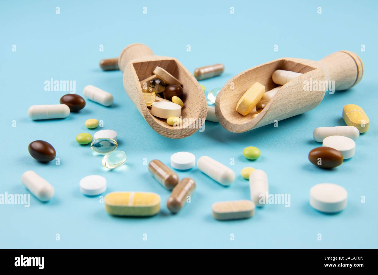 Vista laterale di due cucchiai vintage in legno naturale riempiti di varie pillole e capsule. Messa a fuoco selettiva, sfondo azzurro. Foto Stock