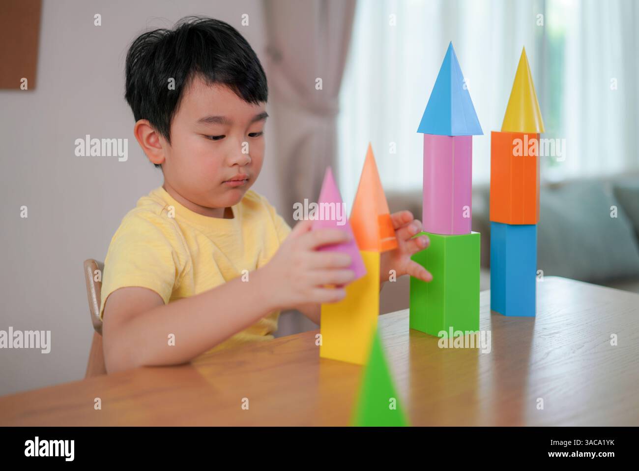 Boy crea delle luminose forme 3D in torri alte, mostrando creatività, concentrazione e gioco iniziale in un ambiente interno rilassato. Foto Stock