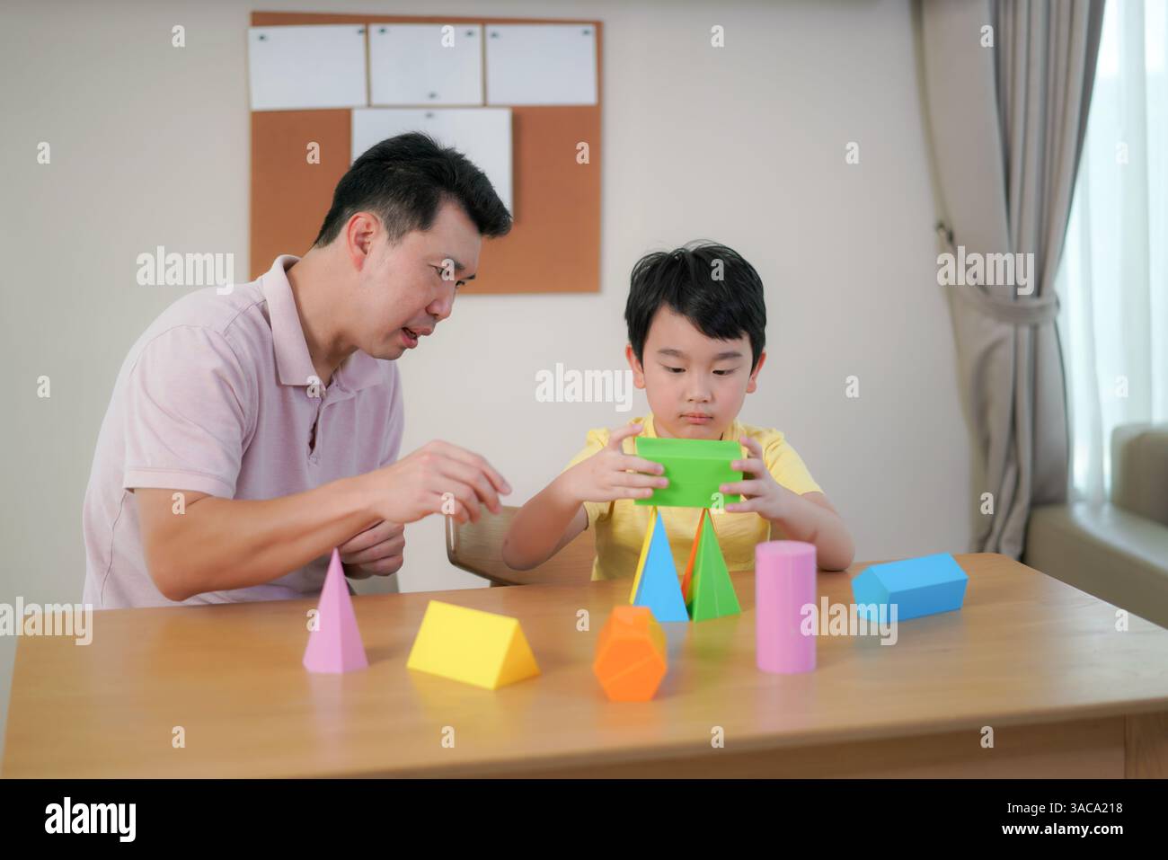 Padre guida suo figlio mentre esplora forme 3D colorate, stimolando la creatività e l'apprendimento precoce DELLE MATERIE prime in un ambiente familiare rilassato. Foto Stock